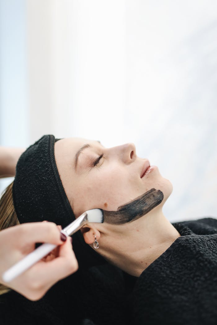 Woman receiving a charcoal face mask at a spa for rejuvenation and relaxation.